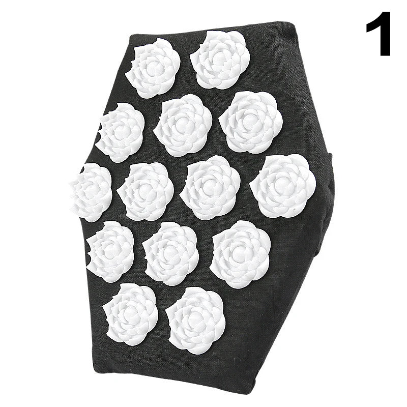 A person is shown using an acupressure massage glove on their back. The glove has a flower-shaped design with raised points, and it appears to be made of black fabric with white accents.